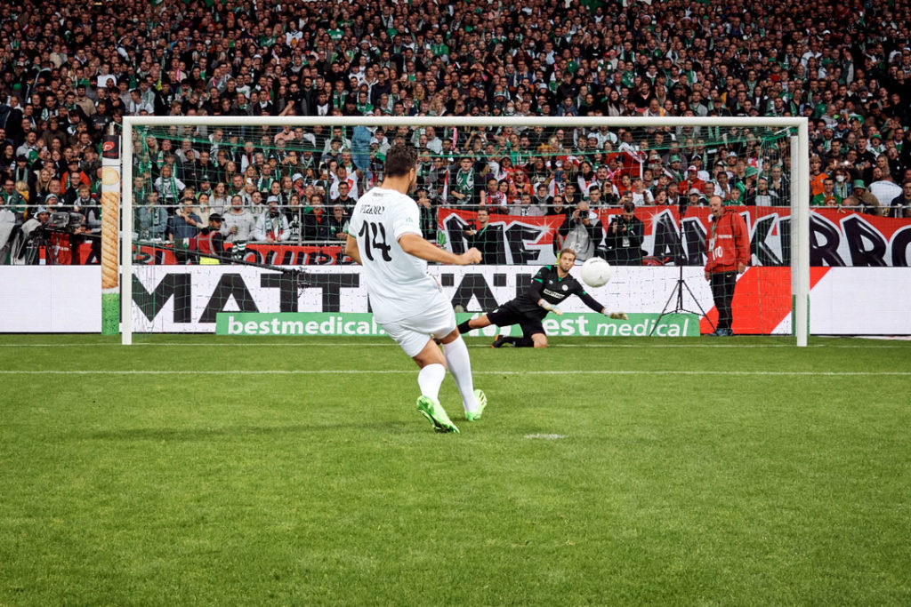 Claudio Pizarro schießt einen Elmeter Strafstoß auf das Tor mit dem Werder Bremen Torwart. Im Hintergrund die best medical Bandenreiter